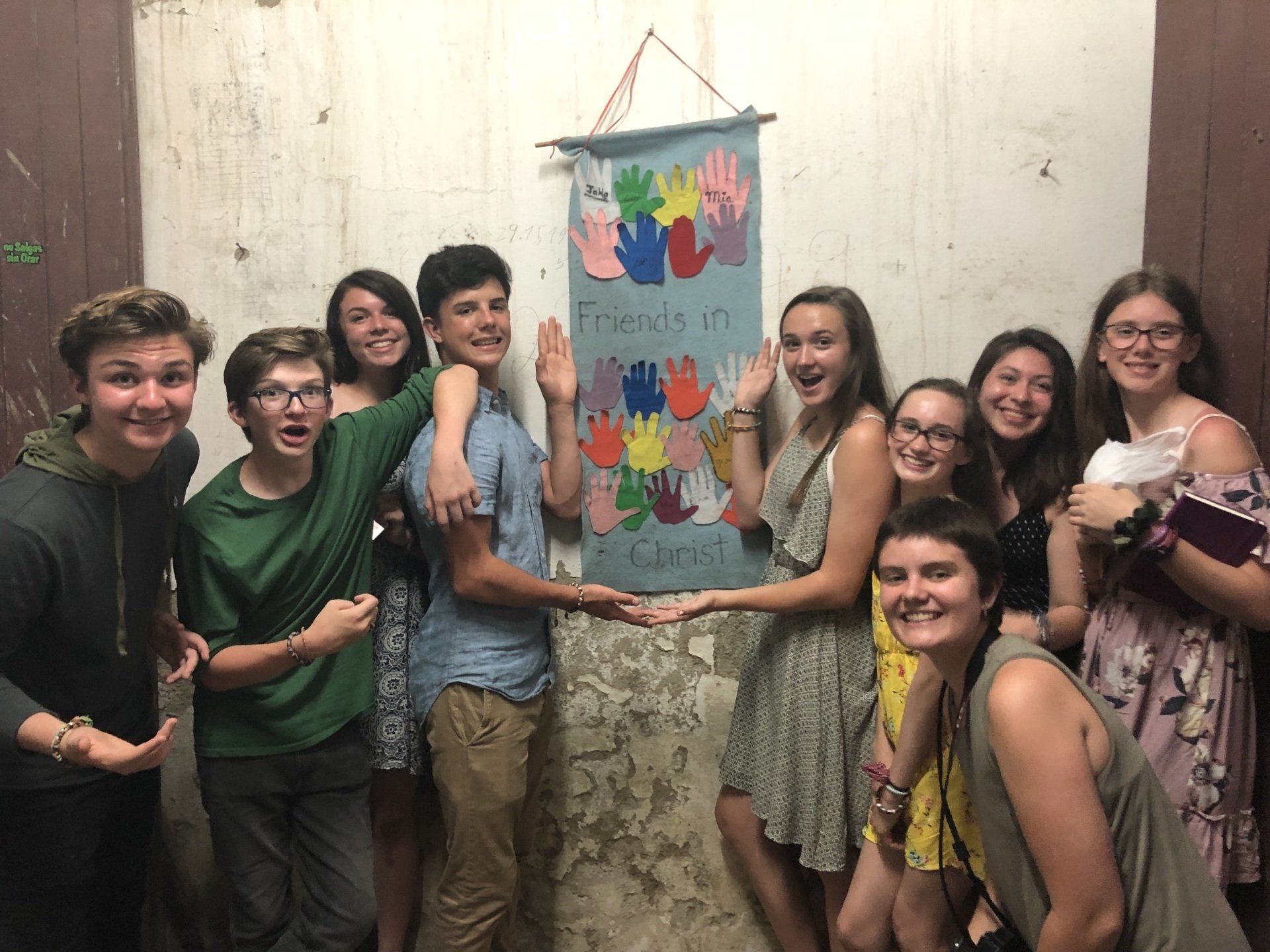 Group of smiling people holding a colorful fabric banner indoors against a plain wall.
