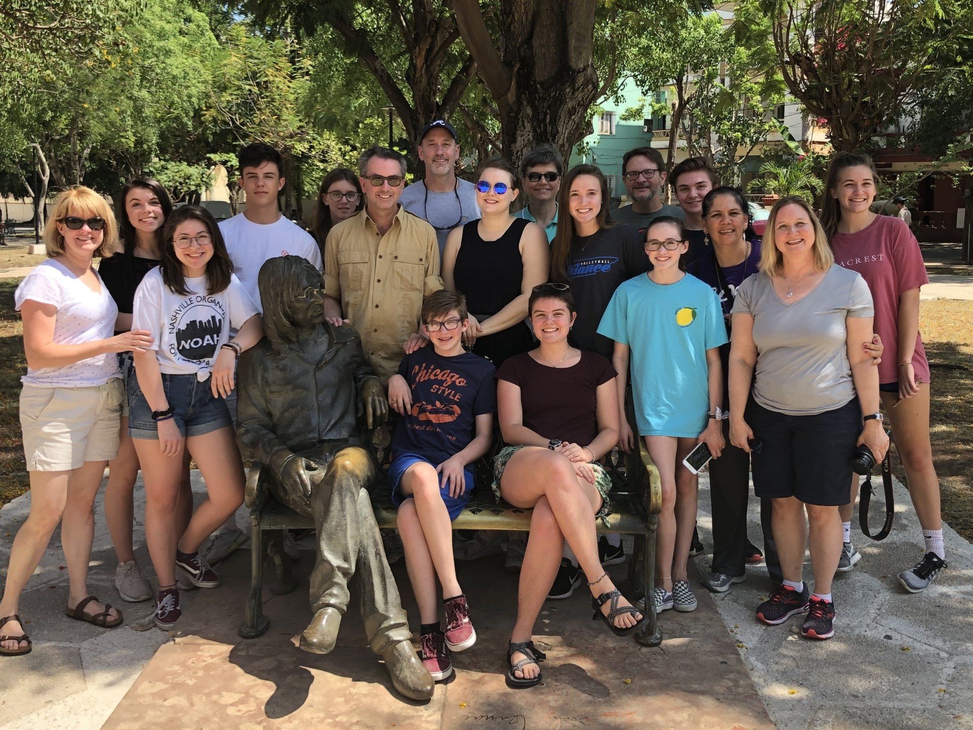 Group posing outdoors with a bronze statue seated in front, trees and stone path in the background