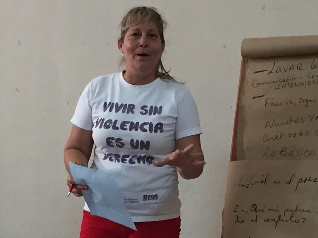 Woman in a white T-shirt speaking beside a flip chart with handwritten notes.