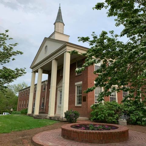 Red-brick church with white columns and steeple, viewed from a landscaped lawn with a circular brick planter.