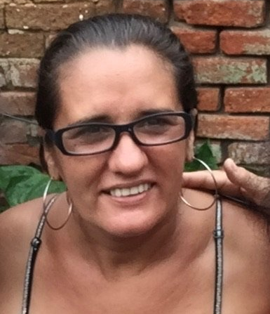 Smiling person wearing glasses and hoop earrings in front of a brick wall