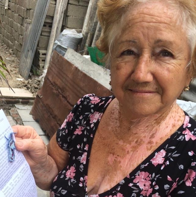 Smiling woman holding a document outdoors beside a fence and wooden planks