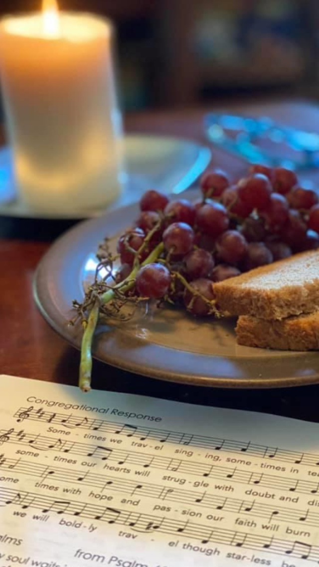 Wine and grapes on a plate beside bread and a handwritten menu, with a candlelit table in the background