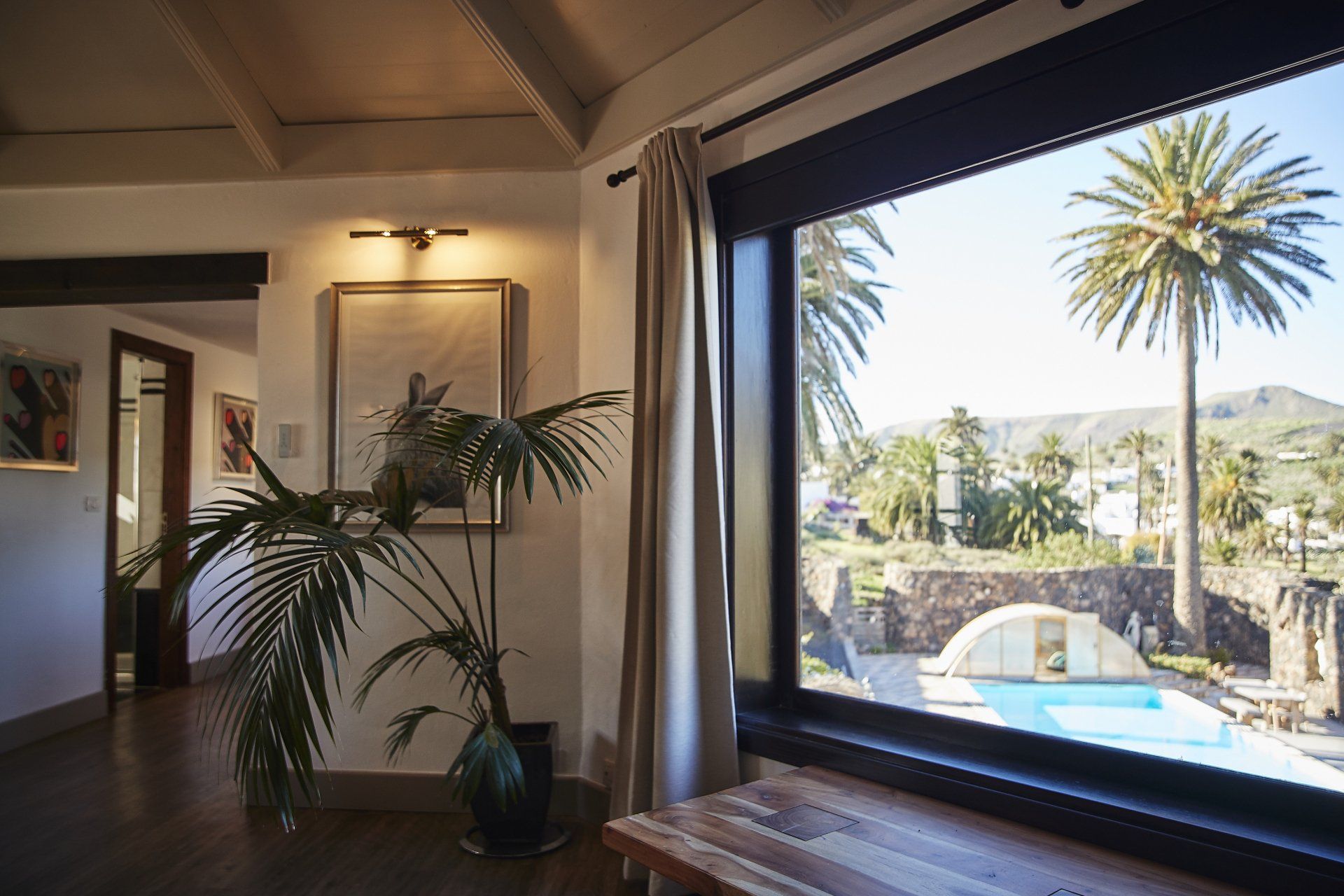 A living room with a large window overlooking a swimming pool and palm trees.