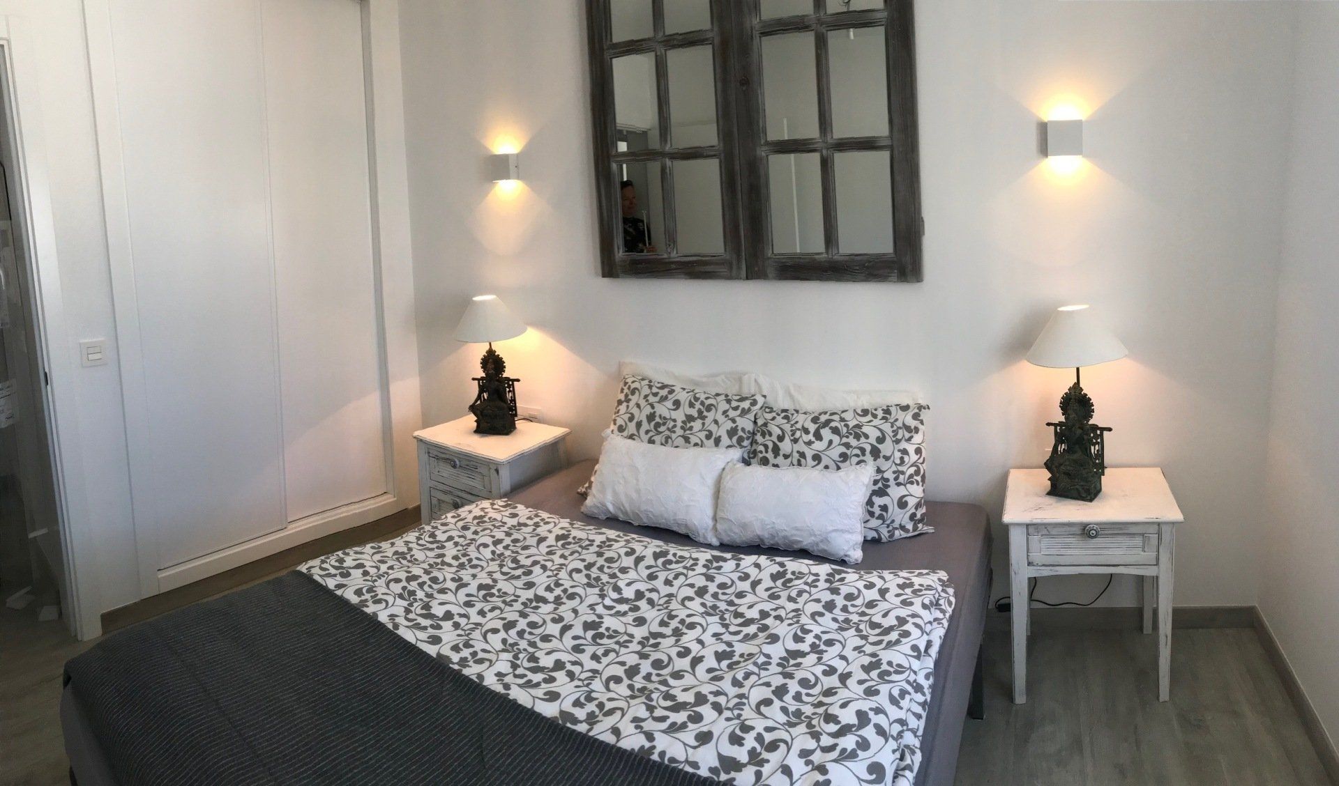 A bedroom with a bed , nightstands , lamps and a mirror.