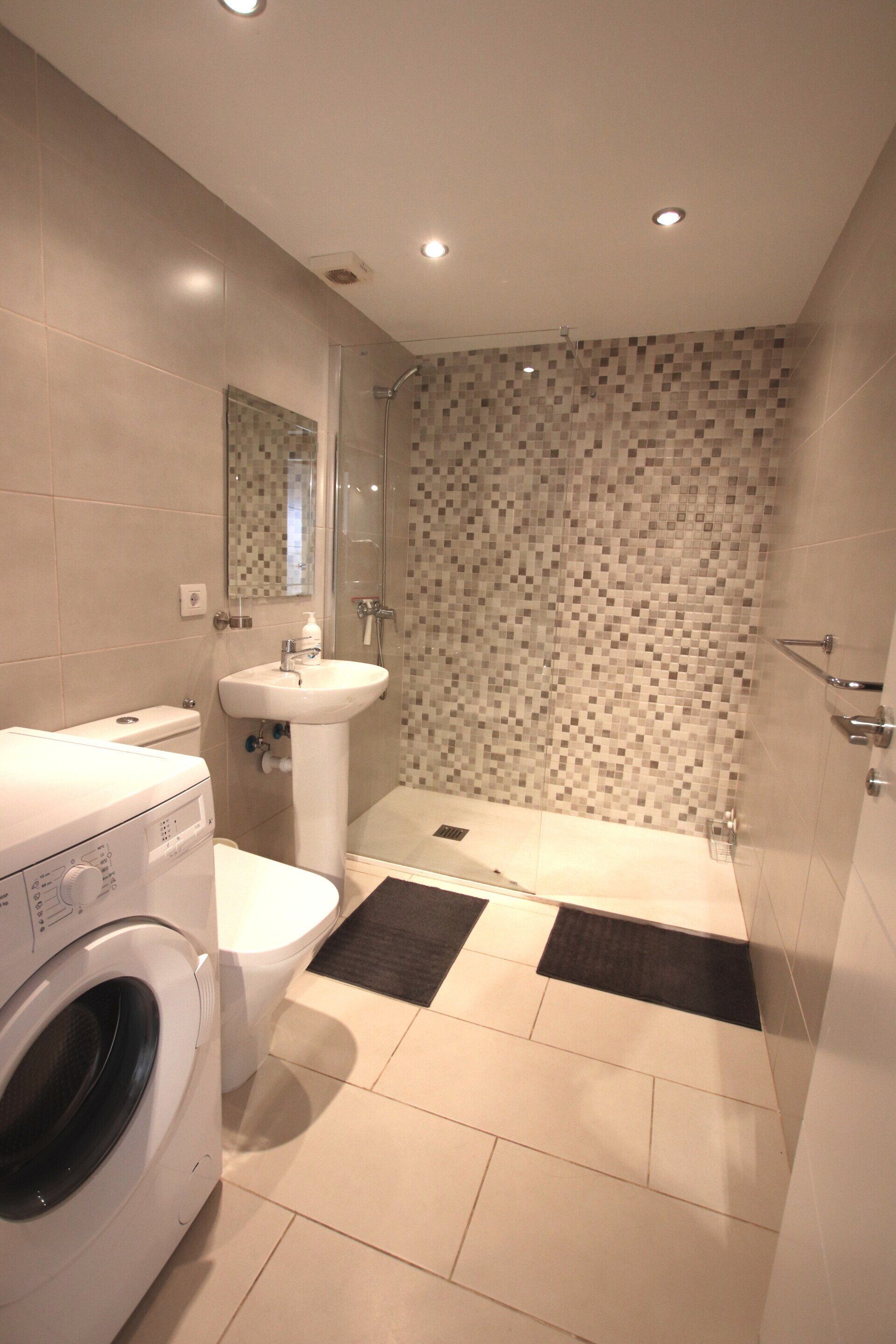 A bathroom with a washing machine , toilet , sink and shower.
