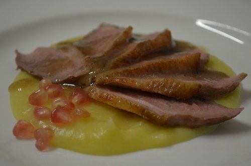 un piatto con delle fette di carne, una mousse gialla e melograno