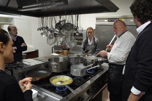 un uomo che indica una pentola in una cucina e altre persone attorno