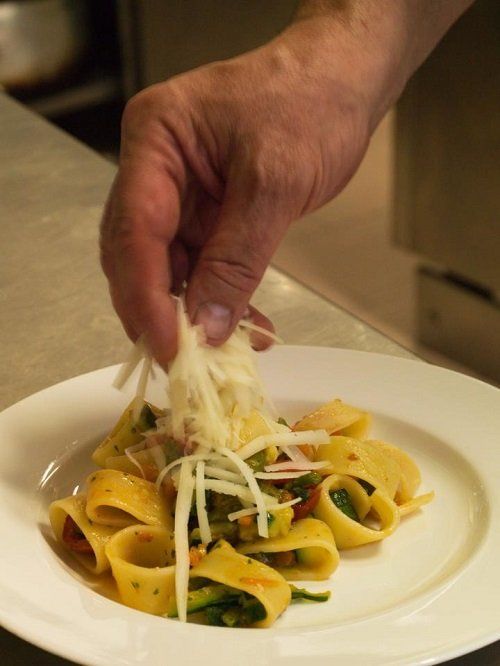 una mano che mette delle scaglie di formaggio su un piatto di pappardelle