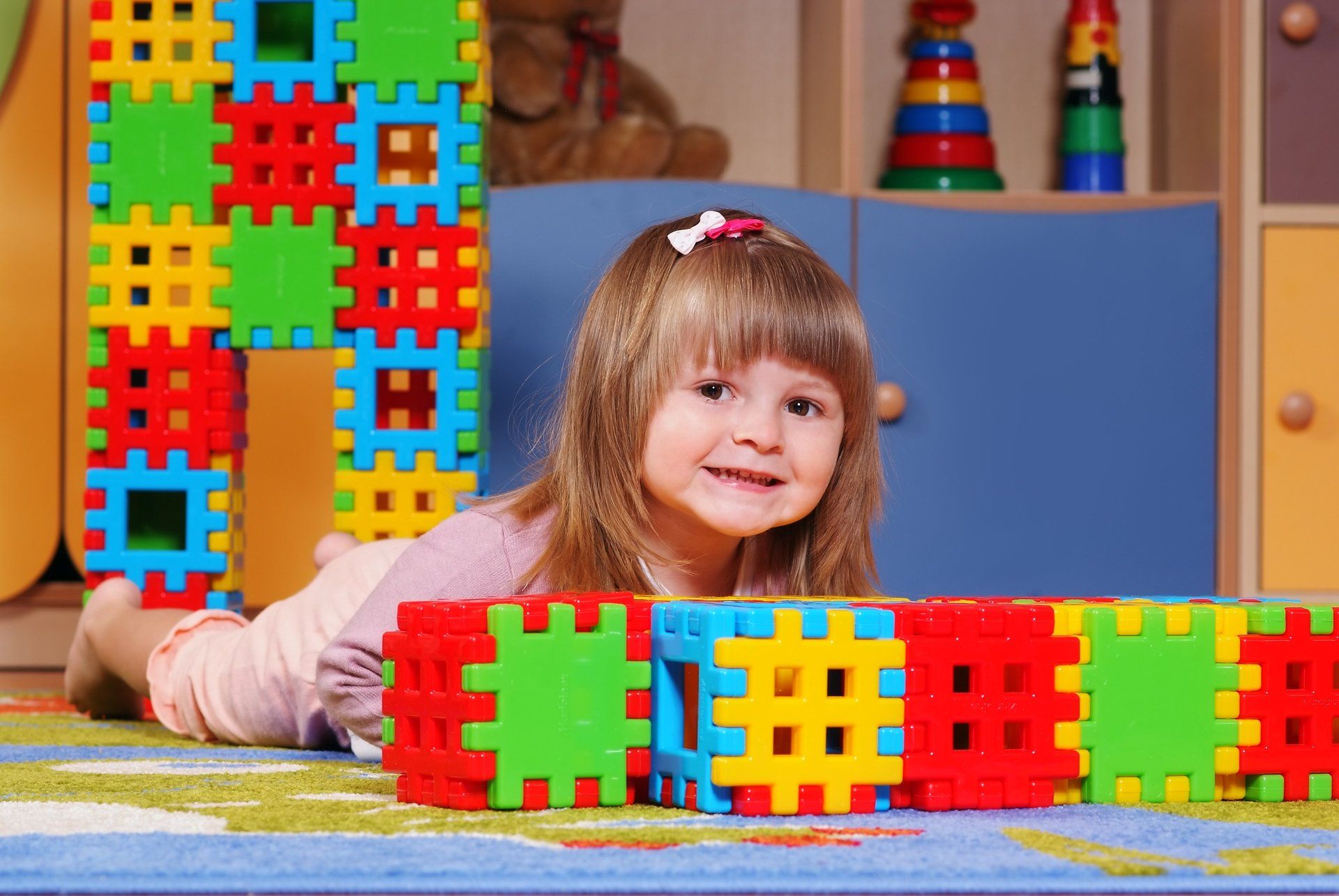 A little girl is laying on the floor playing with colorful blocks.