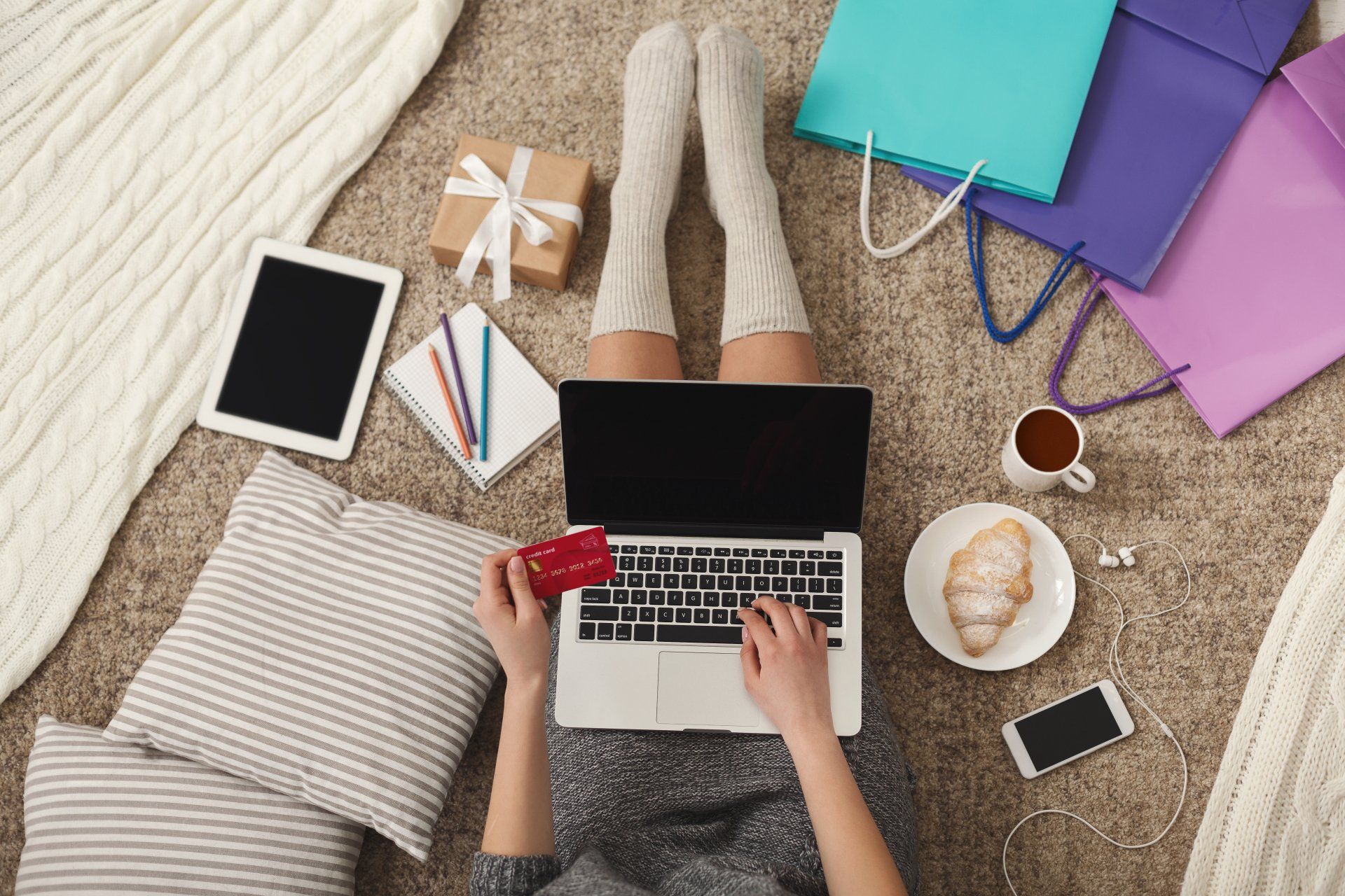 A woman is laying on the floor using a laptop and holding a credit card