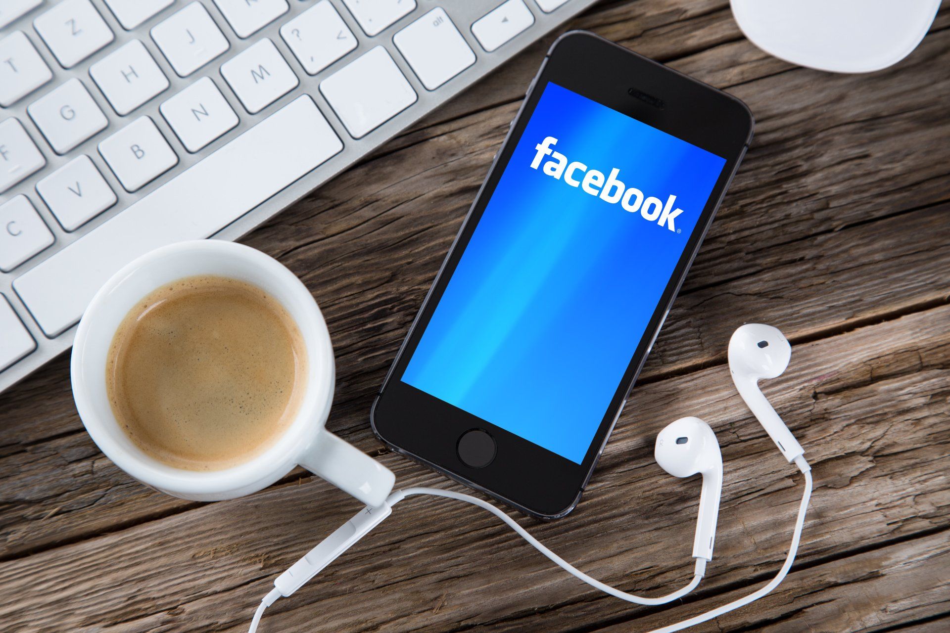 A phone with facebook on the screen next to a cup of coffee