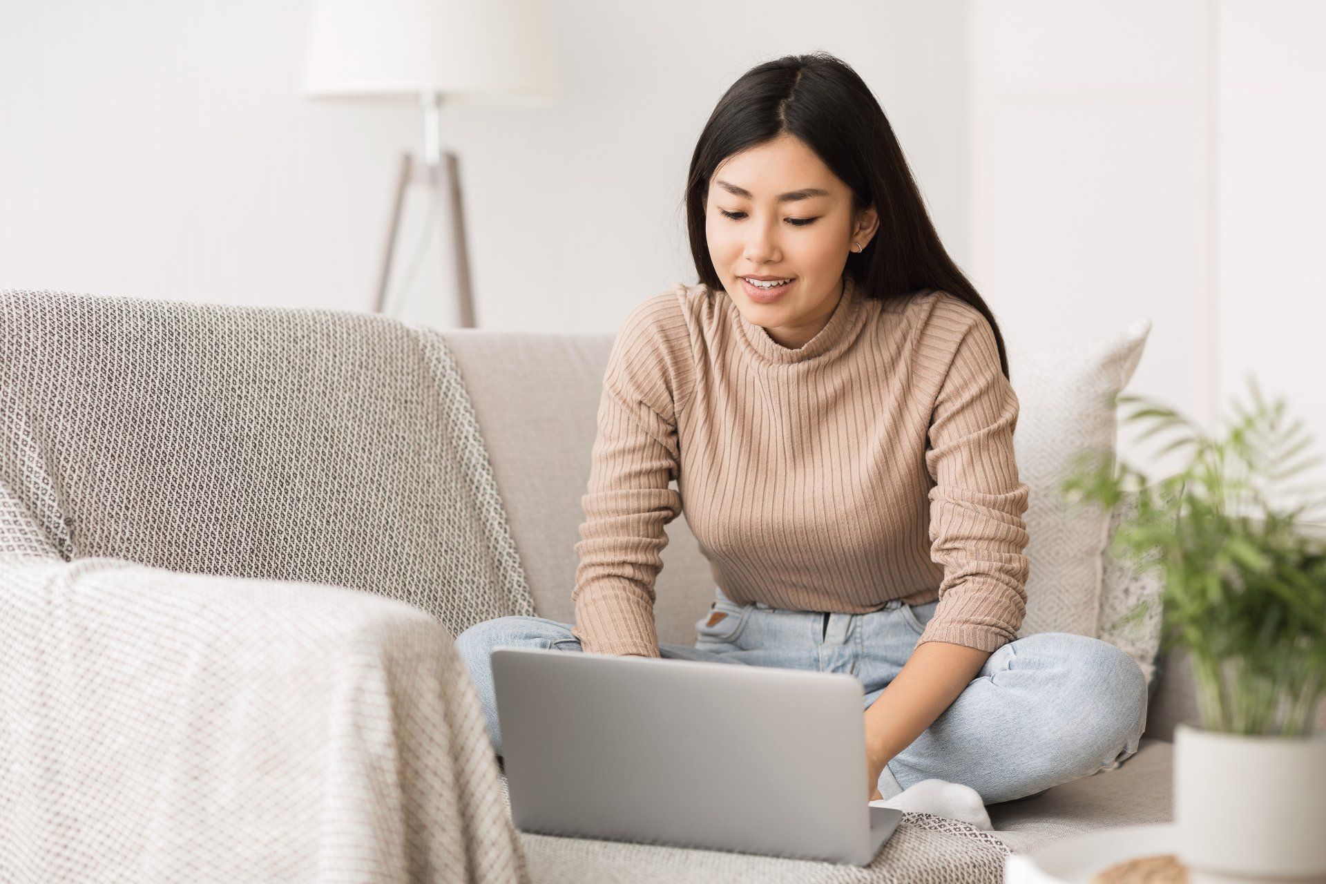 A woman is sitting on a couch using a laptop computer.