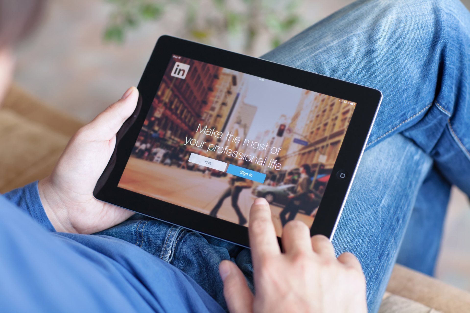 A man is using a tablet with linkedin on the screen