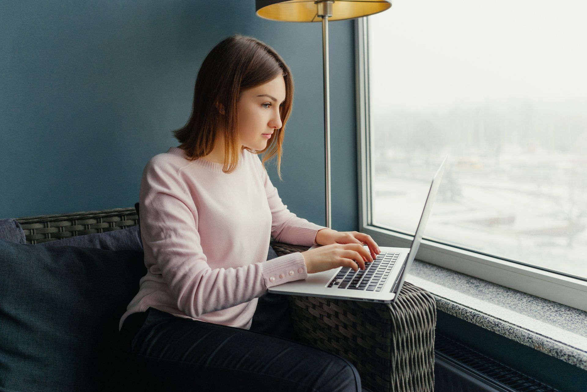 A woman is sitting in front of a window using a laptop computer.