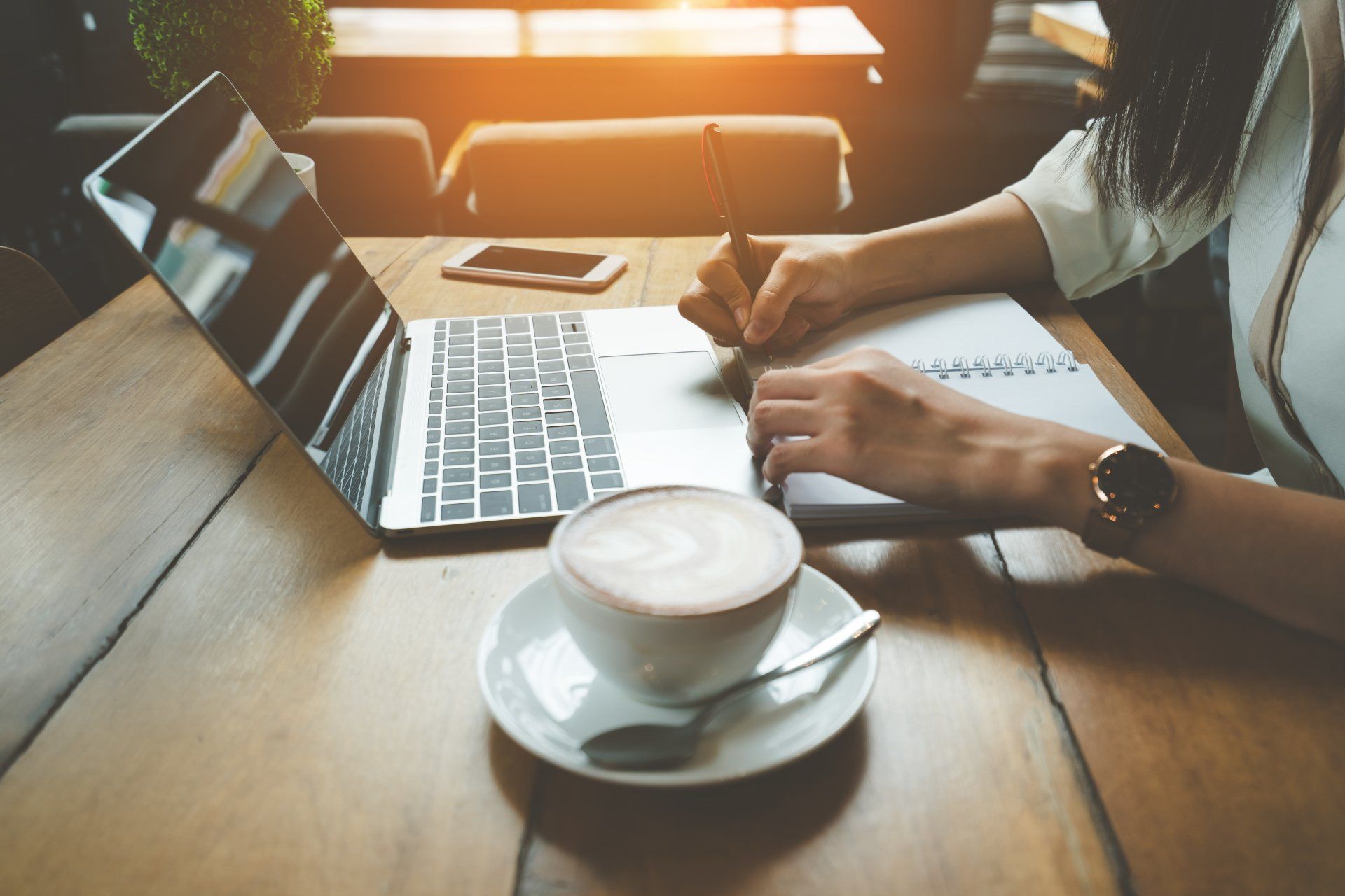 A woman sits at a table with a cup of coffee and a laptop