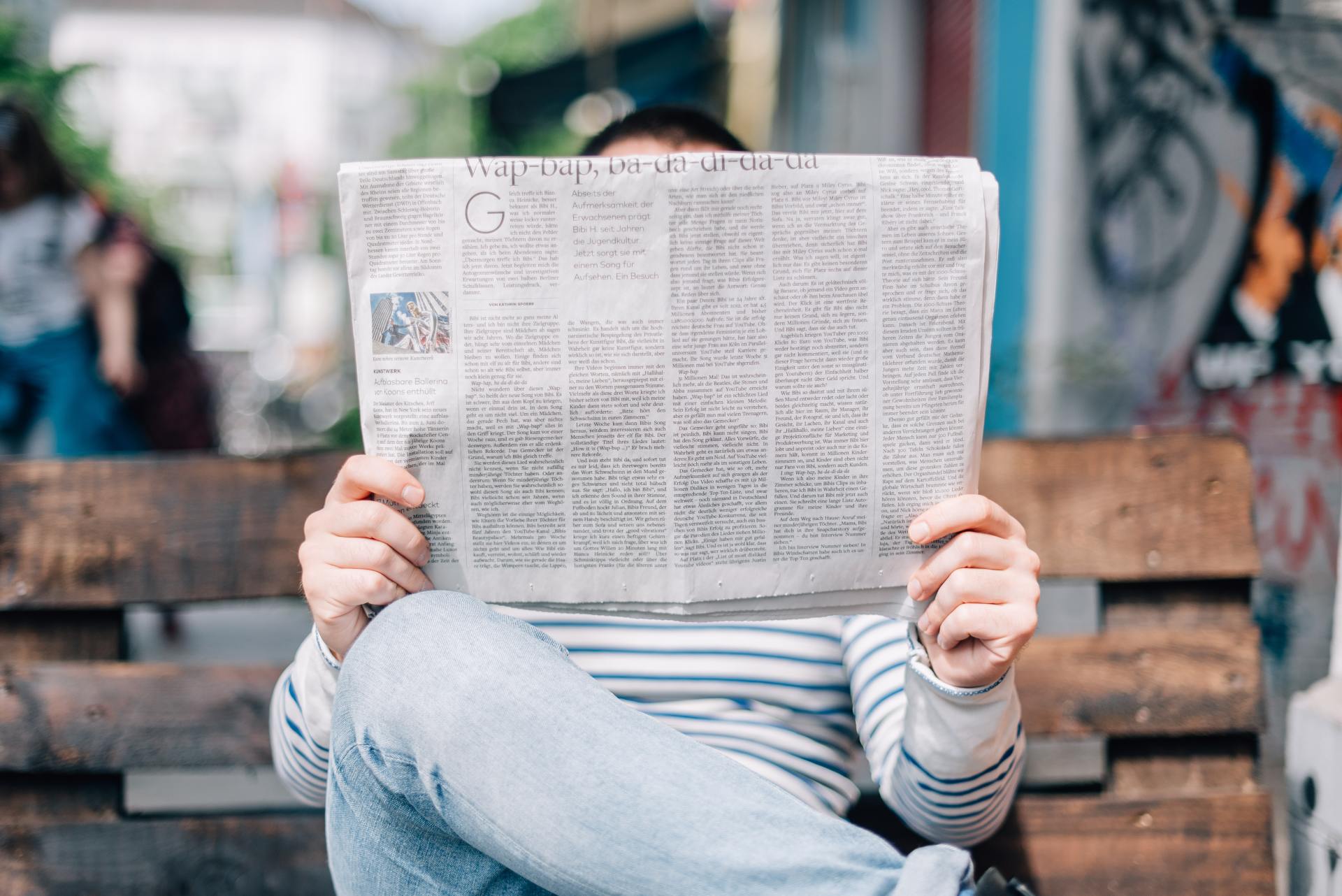 A person is sitting on a bench reading a newspaper