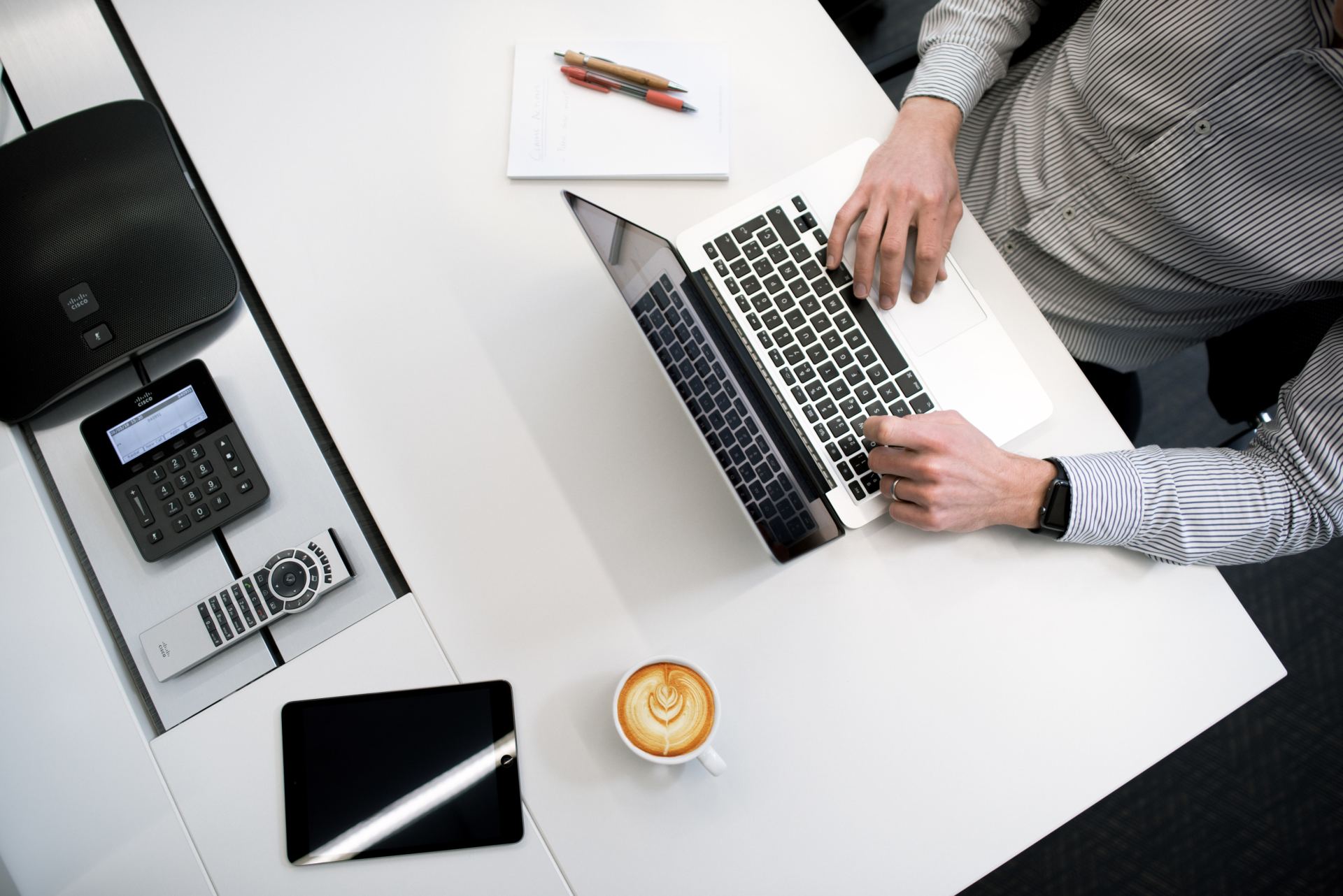 A man is typing on a laptop next to a cup of coffee