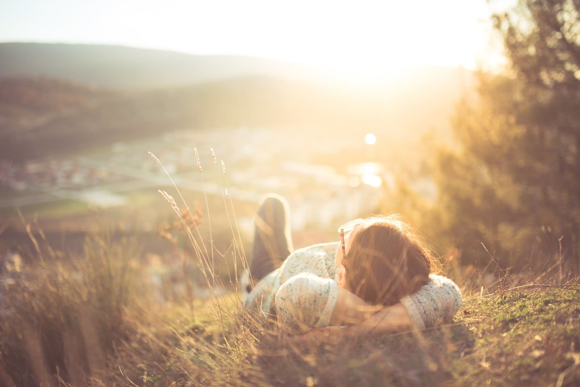 Eine Frau und ein Hund liegen bei Sonnenuntergang im Gras auf einem Hügel.