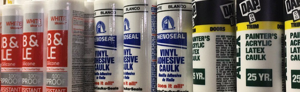 Caulk tubes lined up on a shelf with red and white labels.