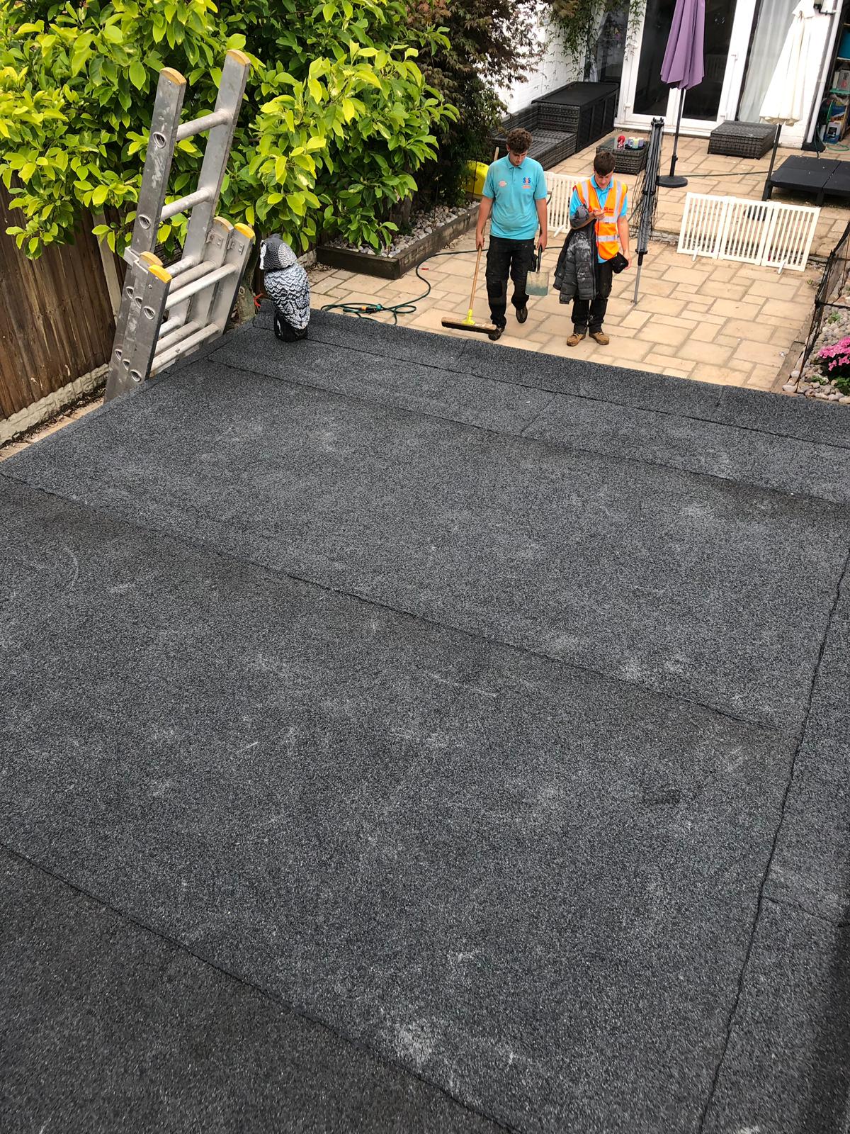two men standing on a roof with a ladder in the background