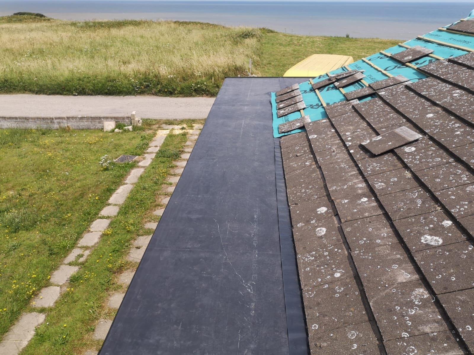 a roof with shingles on it and a yellow boat in the background