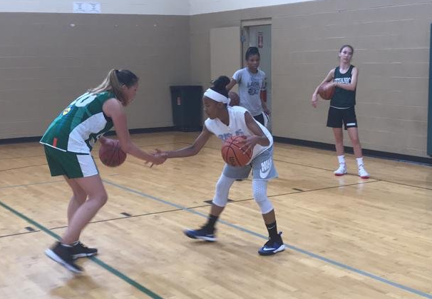 A group of girls are playing basketball in a gym and one of the girls has the number 5 on her jersey