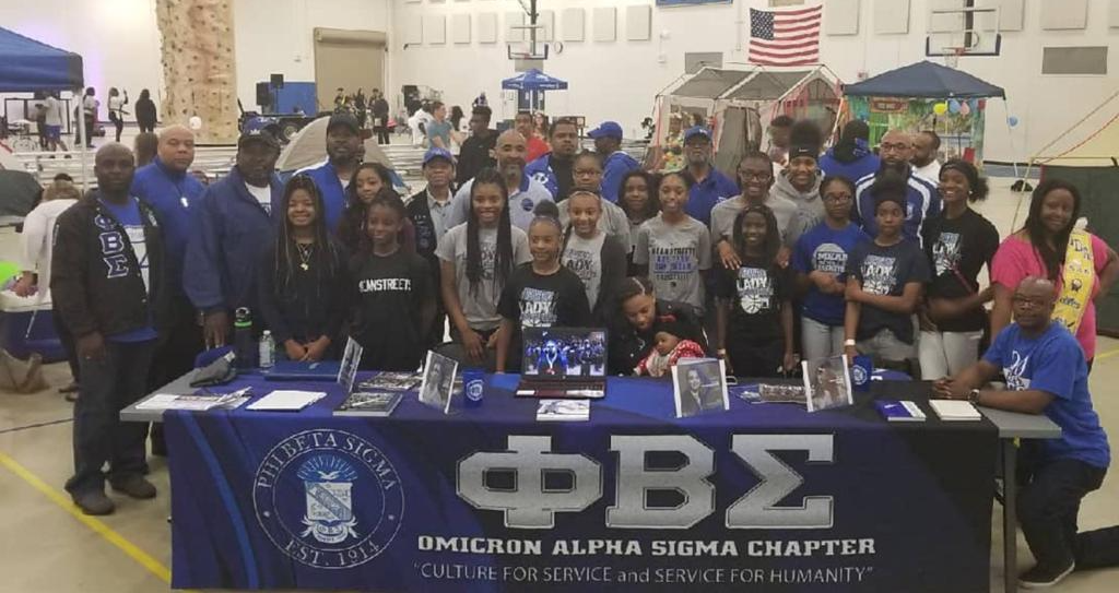 A group of people standing around a table with a banner that says fbs