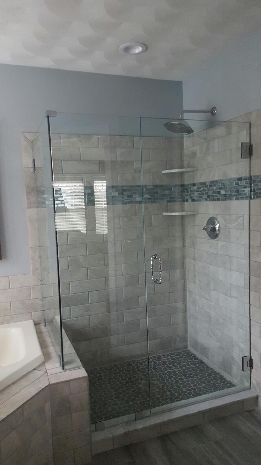 Glass shower enclosure with stone tile and accent stripe in a bathroom.