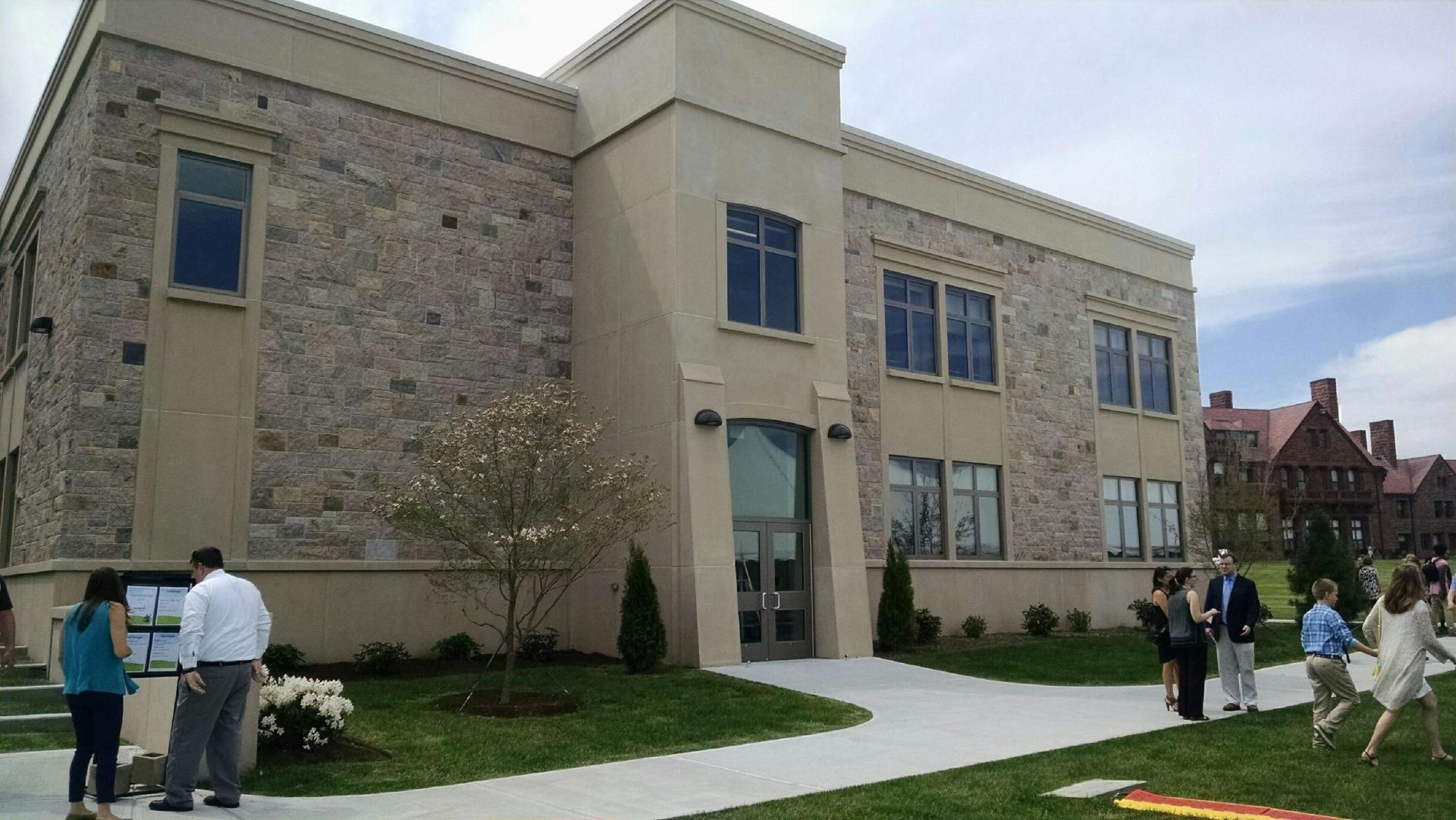 Modern stone building with people on the lawn, sunny day.