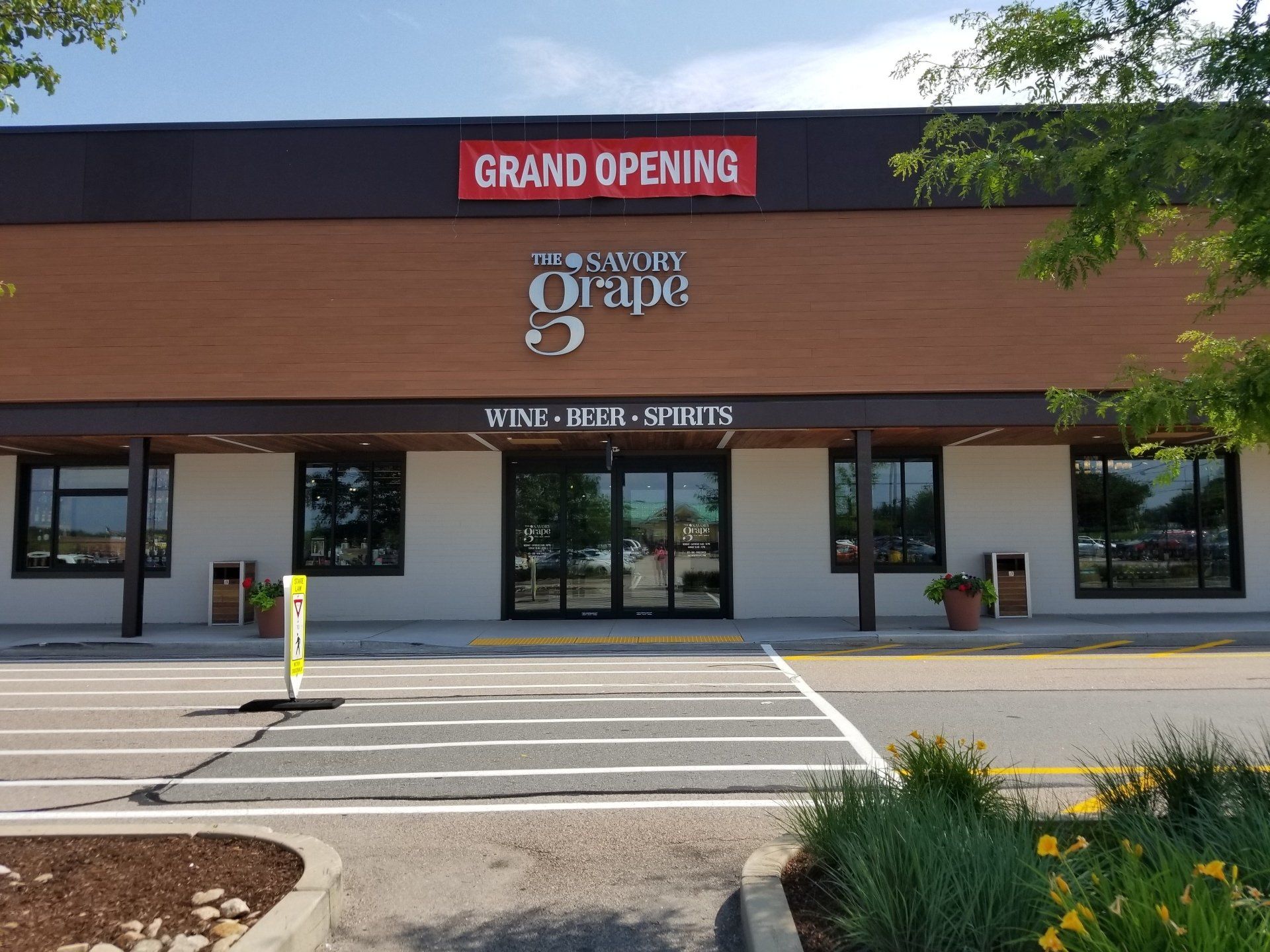 Grand opening of The Sour Grape wine store; brown building, red sign, storefront.