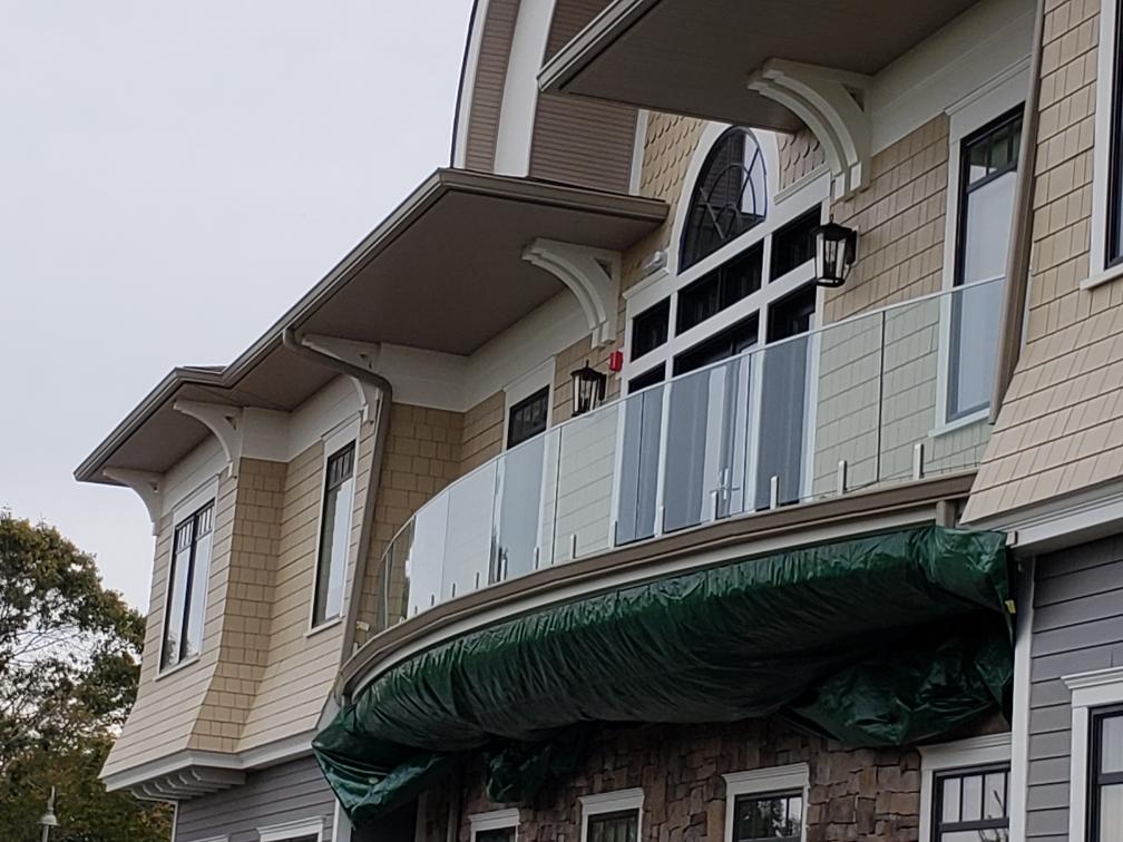 A building with curved rooflines, tan and grey siding, glass balconies covered in green tarps.