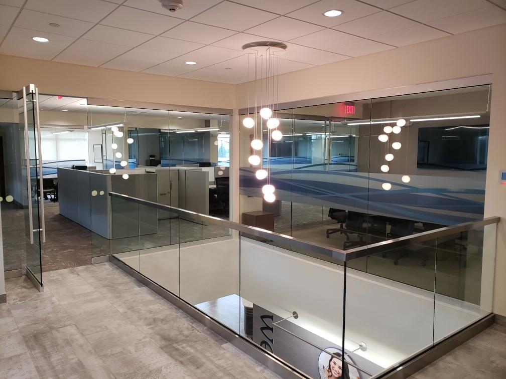 Modern office interior with glass walls, stainless steel railings, and a decorative light fixture.