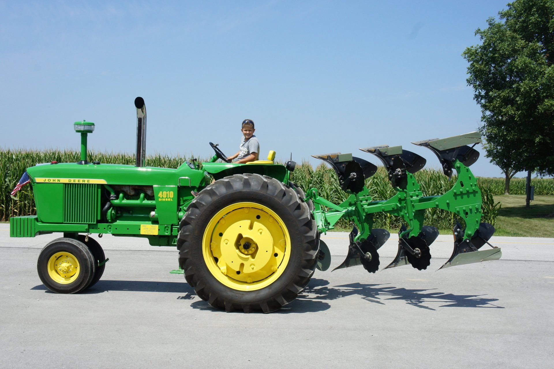 Green John Deere tractor with plow in a field, driver at the wheel.