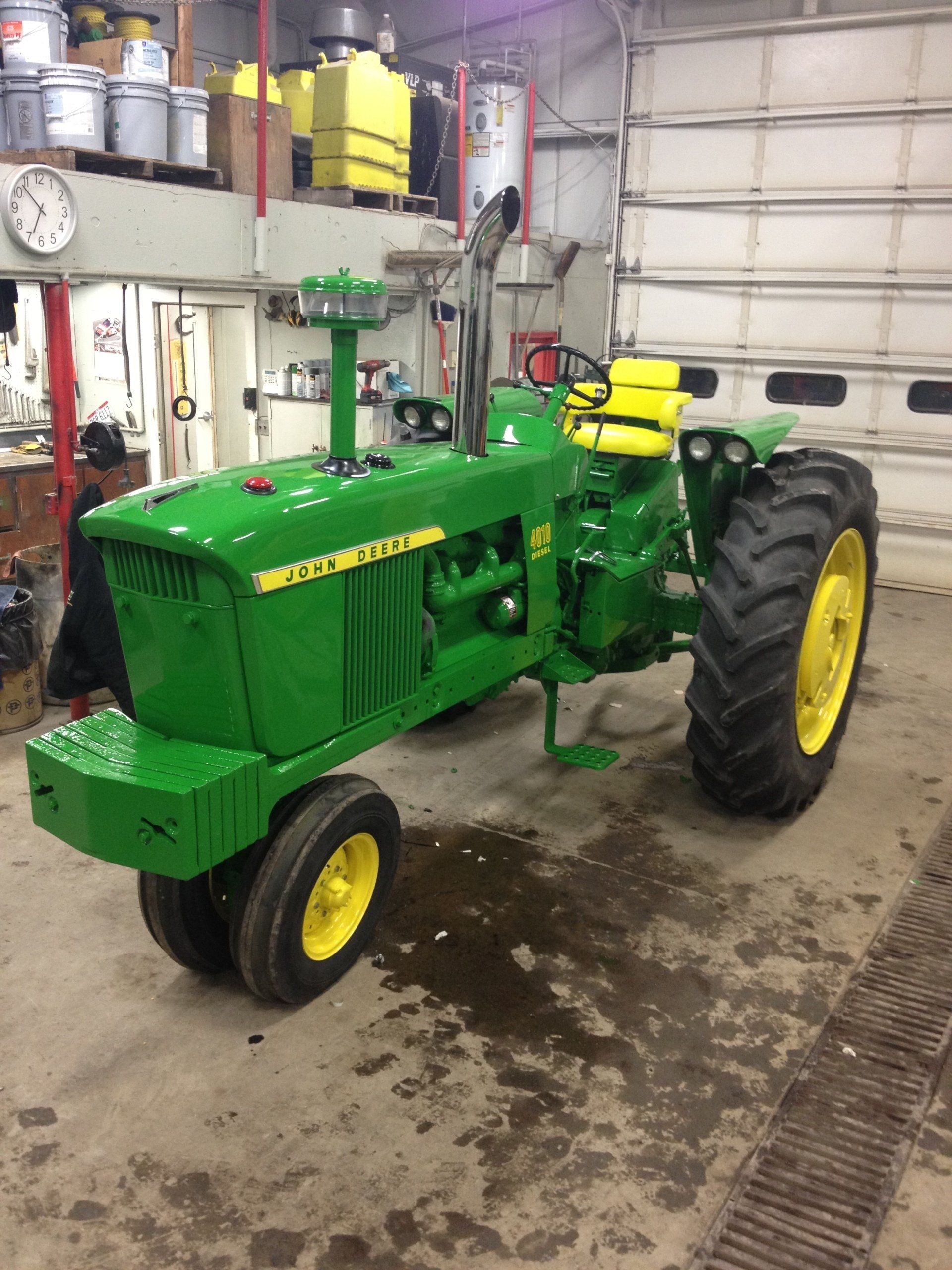Green John Deere tractor with yellow wheels, parked inside a garage.
