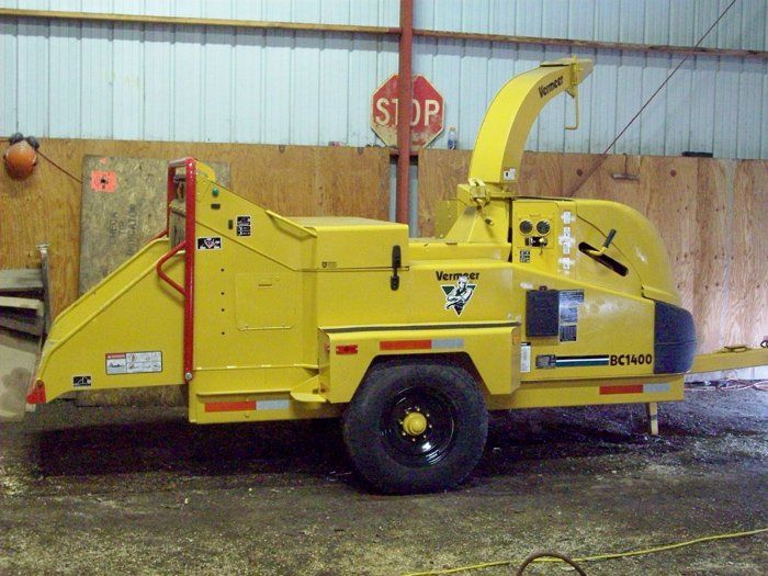 Yellow Vermeer wood chipper on a trailer, parked inside a building with a stop sign.