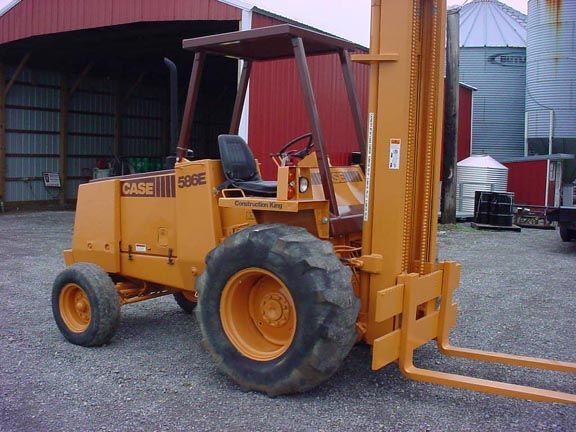 Orange Case 585E forklift parked outside, next to red building.