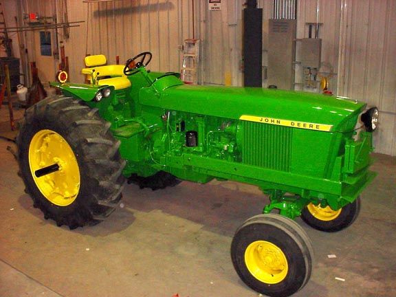 Green and yellow John Deere tractor, front view. Brightly painted, set in a building.