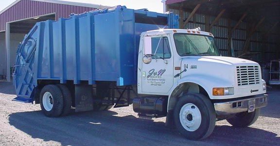 Blue and white garbage truck parked outside a building.