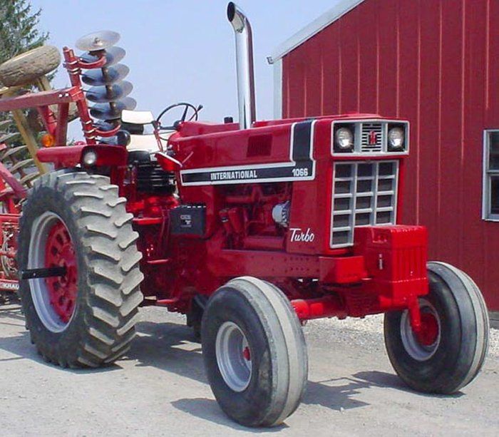 Red International 1066 Turbo tractor with attached farm implement, parked in front of a red building.
