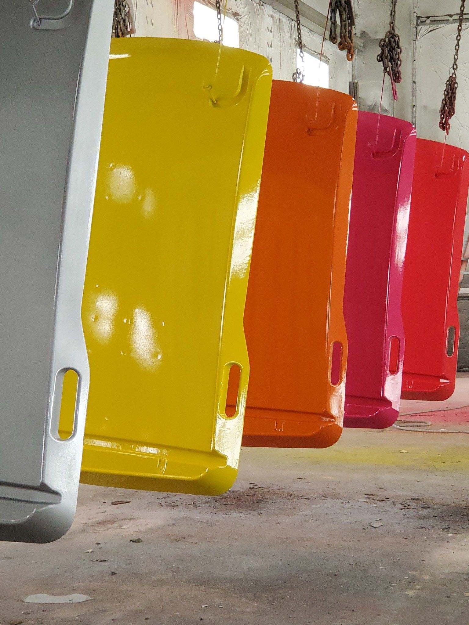 Row of colorful panels, each freshly painted in gray, yellow, orange, pink, and red, hanging in a factory setting.