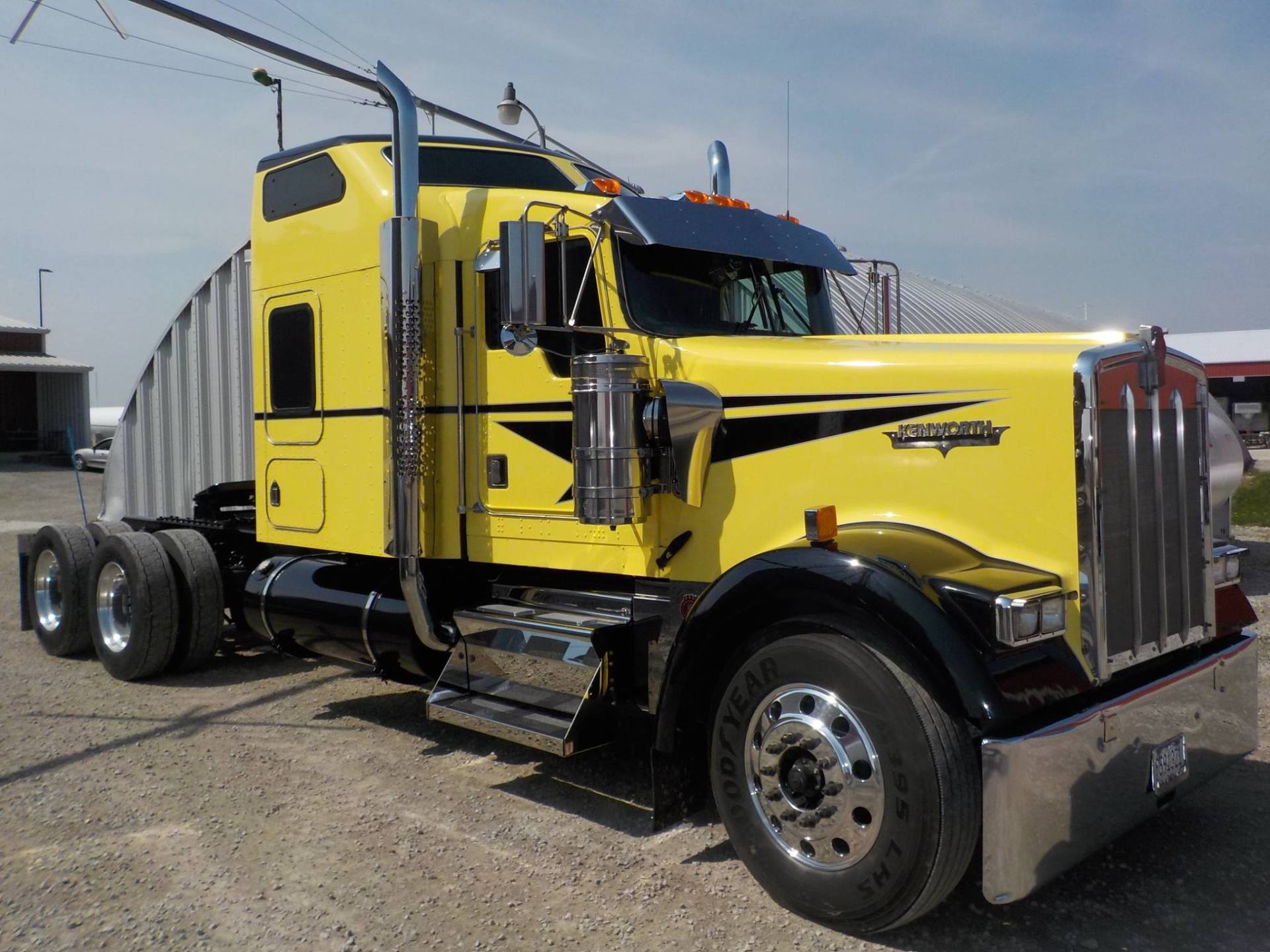 Yellow Kenworth semi-truck with chrome accents parked on a gravel surface.
