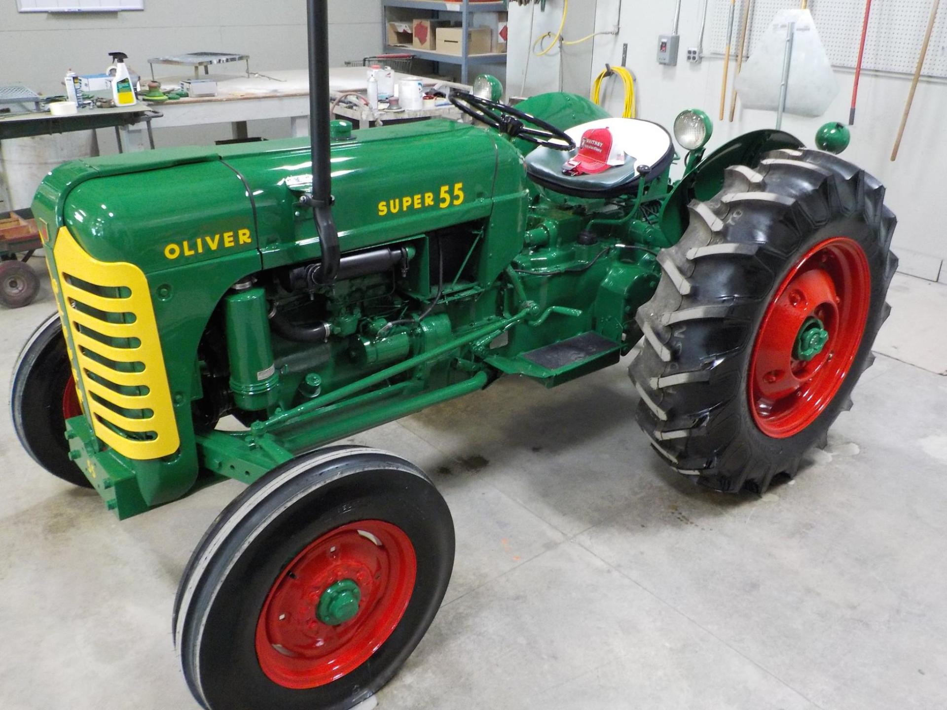 Green and yellow Oliver Super 55 tractor with red wheels, indoors.