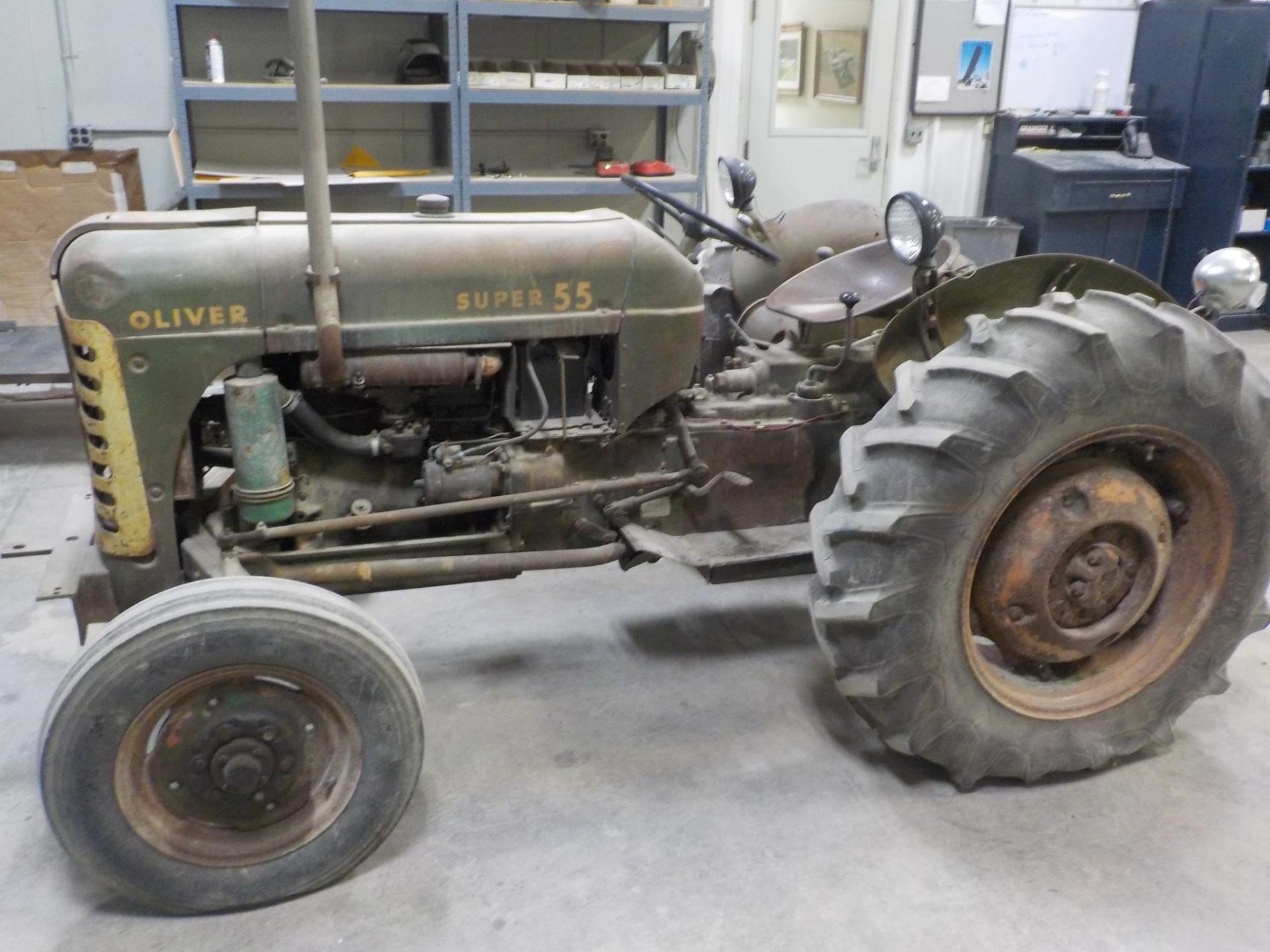 Olive green Oliver Super 55 tractor with worn tires in a workshop setting.