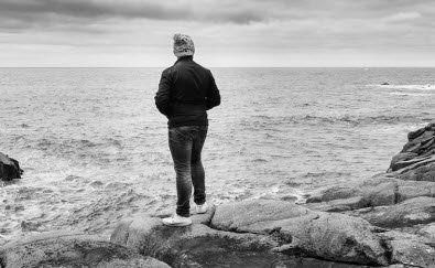 A man is standing on a rock overlooking the ocean.