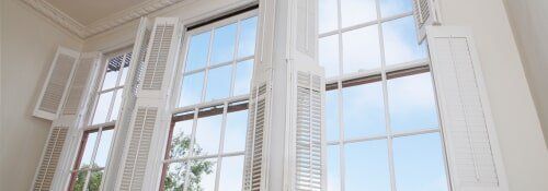 White interior window with open shutters, blue sky visible.