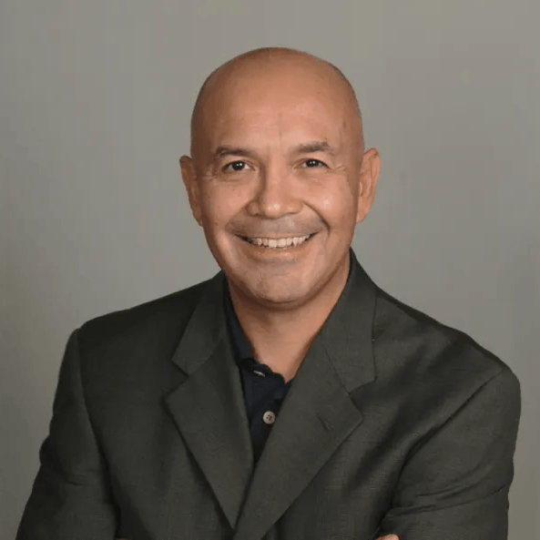 Smiling bald man in a dark suit posing against a plain gray background
