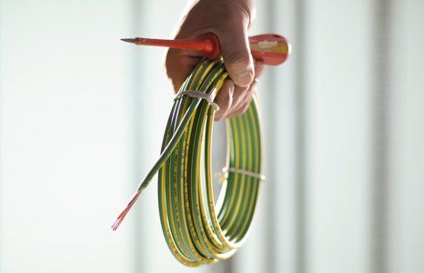 a hand holding electrical cable and screw driver
