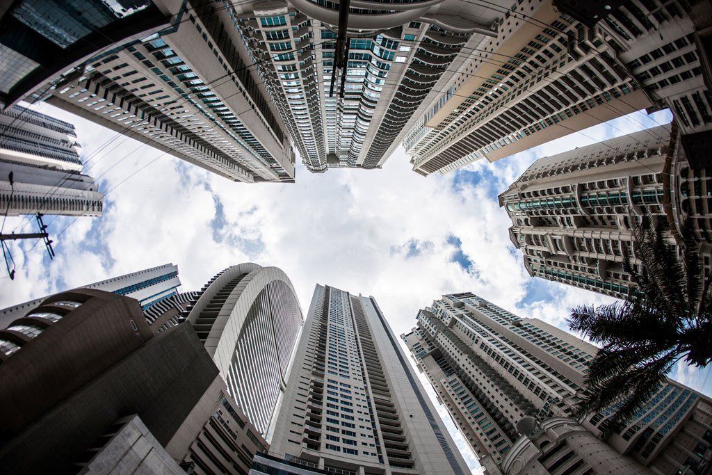 Looking up at a bunch of tall buildings against a cloudy sky