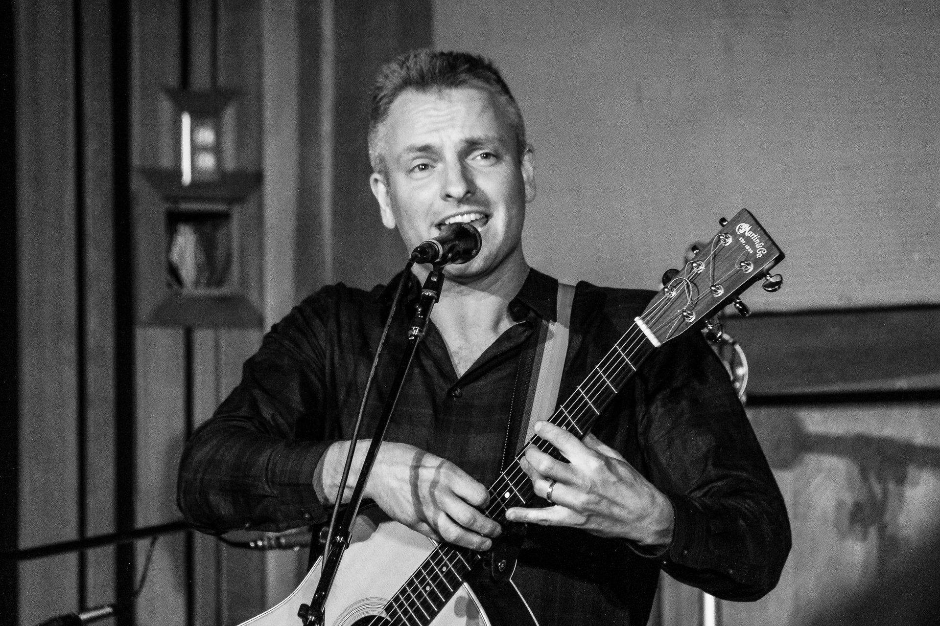 A man is singing into a microphone while holding a guitar.